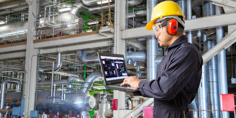 Maintenance technician using IoT asset management tools to monitor industrial equipment performance on a laptop