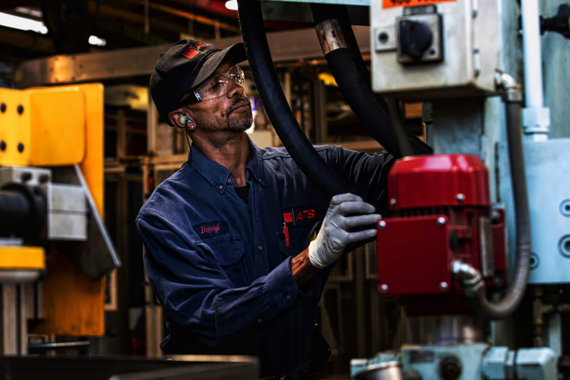 Industrial technician performing hands-on equipment maintenance inspection in a manufacturing facility